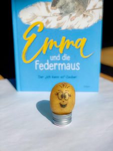 Kartoffel mit ausgezeichnetem Gesicht & Federmaus-Buch im Hintergrund 